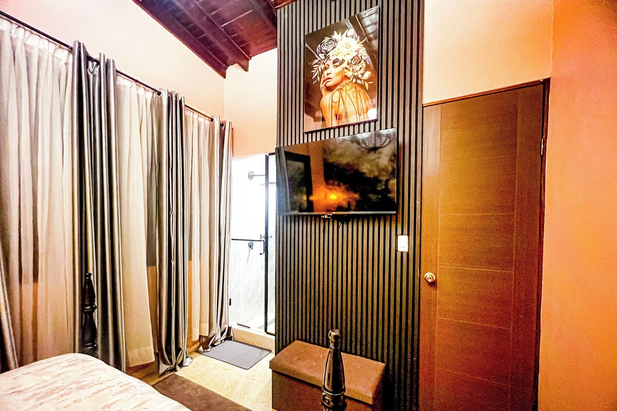 A hotel room with a bed, a small bench, a door, and a wall-mounted television.