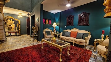 Uma sala de estar luxuosa com móveis ornamentados, um tapete vermelho e arte decorativa nas paredes.