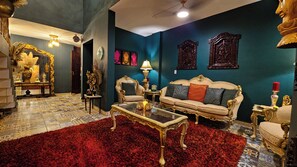 Un salon luxueux, agrémenté de meubles richement décorés, d’un tapis rouge et d’œuvres d’art ornementales accrochées aux murs.