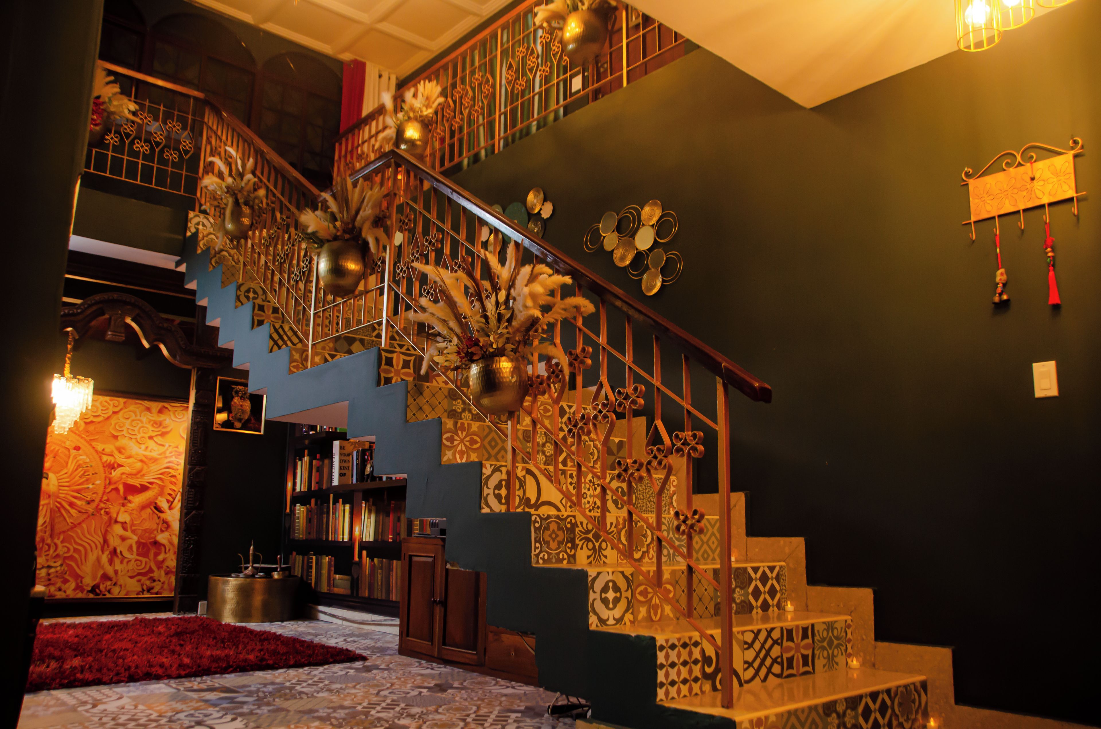 Una escalera con barandillas metálicas ornamentadas y peldaños estampados, rodeada de estanterías y una alfombra roja.