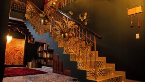 Un escalier orné de rampes en métal décoratif et de marches à motifs, entouré d’étagères et surmonté d’un tapis rouge.