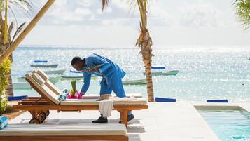 Un espace aménagé au bord de la piscine, avec des chaises longues et une personne vêtue de bleu qui nettoie une chaise.