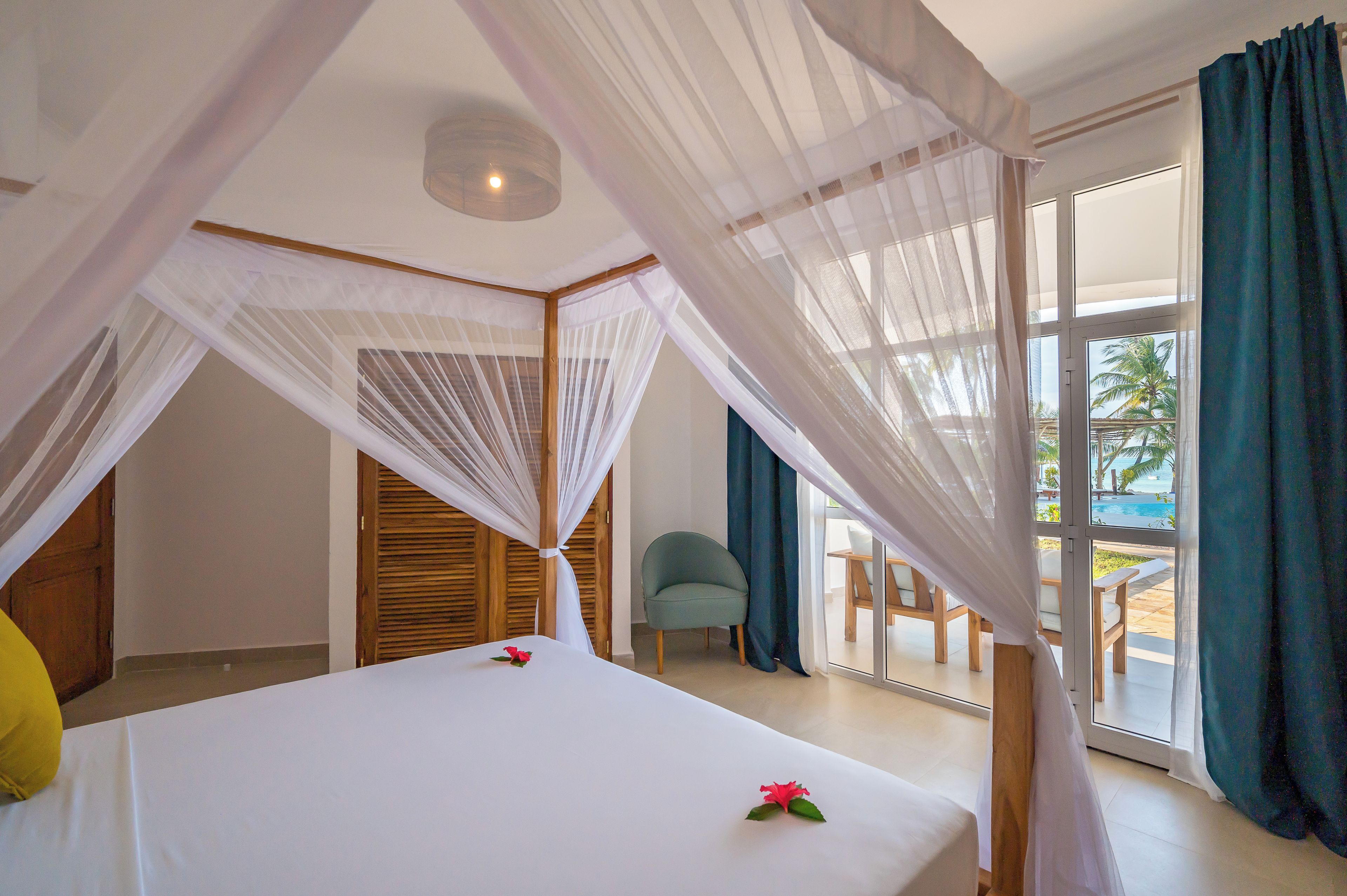 A bedroom with a canopy bed, a view of the pool, and a chair by the window.