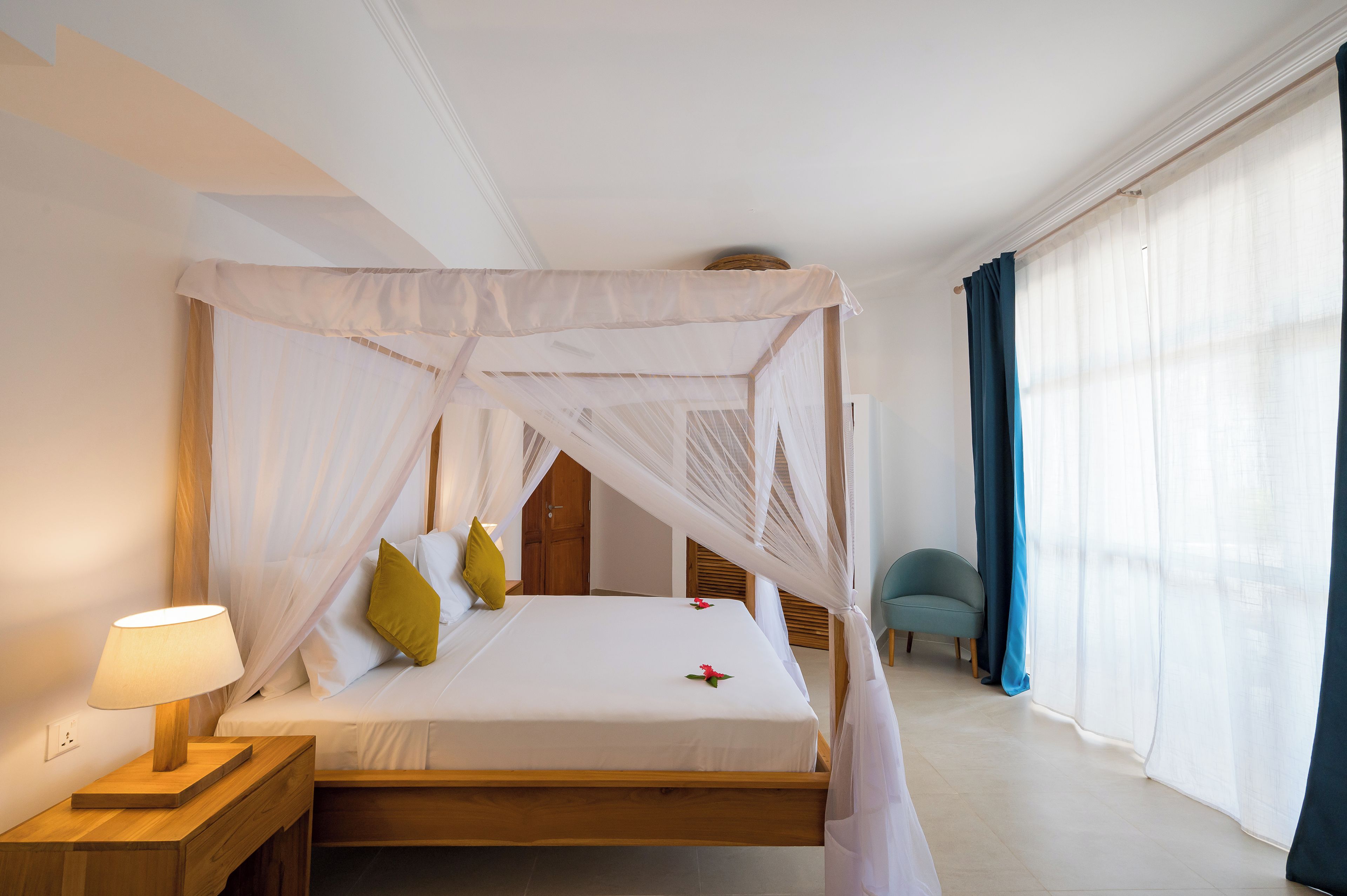 Un lit à baldaquin, une table de chevet avec une lampe et une chaise dans une chambre d’hôtel.