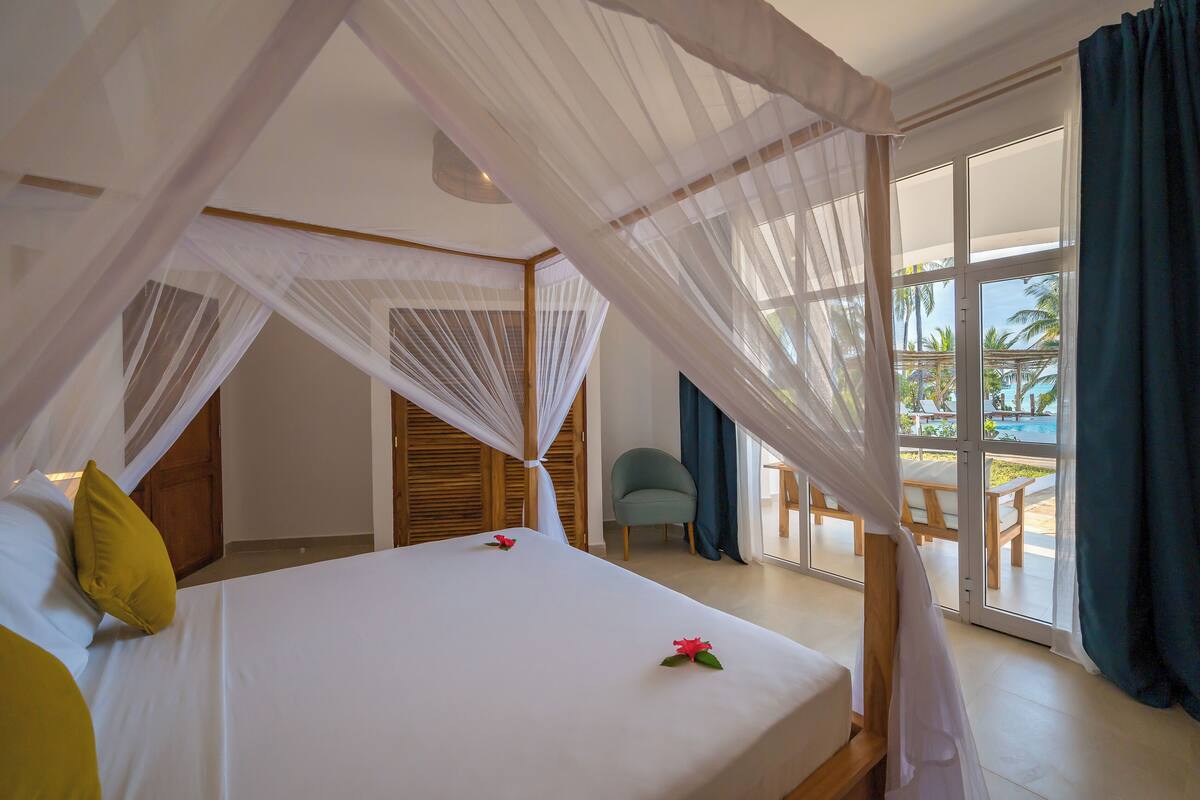 Un dormitorio con cama a dosel, vistas al área de la piscina exterior y una puerta que da a otra habitación.