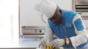 Un chef vêtu d’un uniforme bleu et d’un chapeau blanc prépare des plats sur un plan de travail en acier inoxydable.