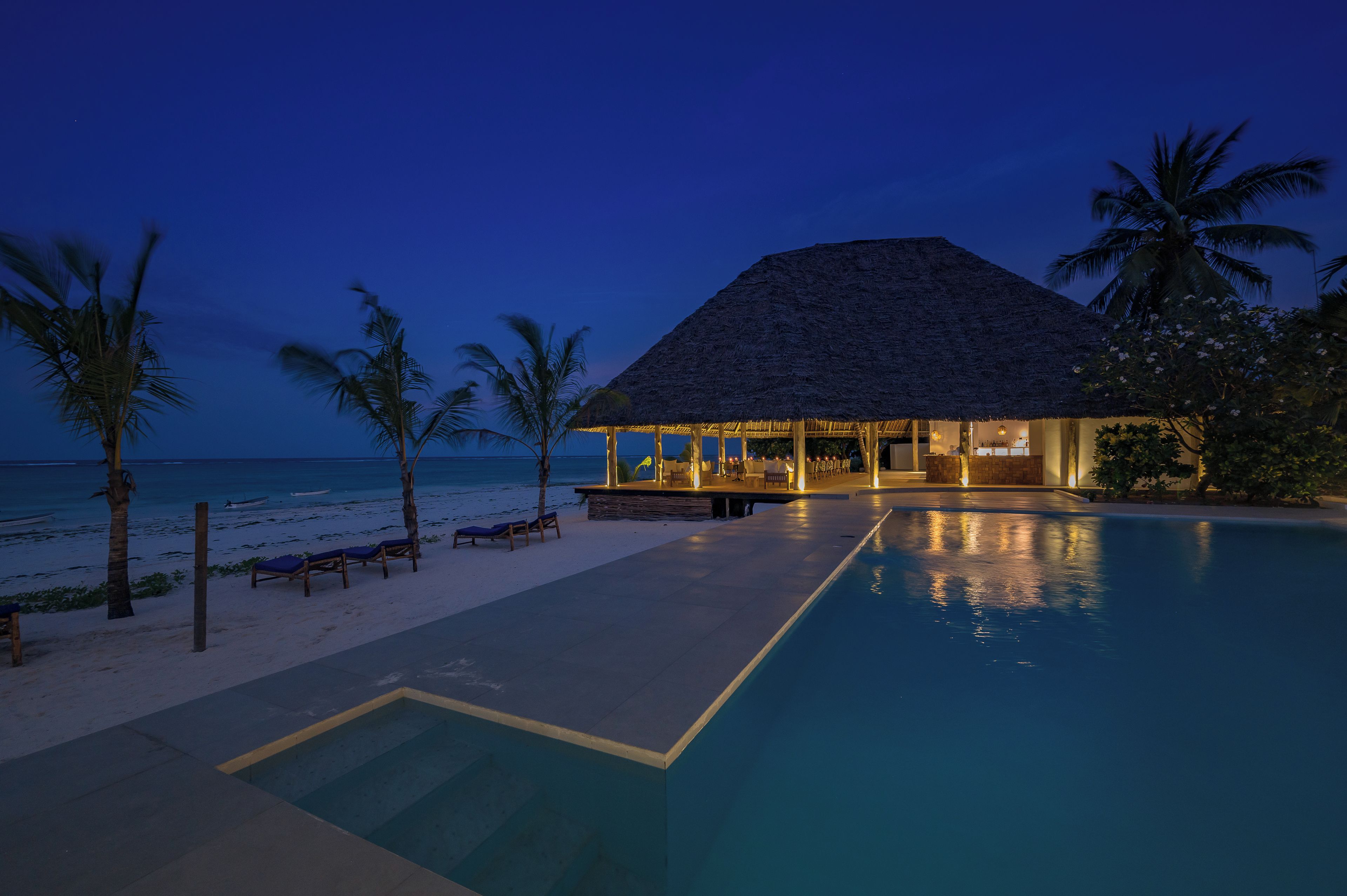 A resort with a pool, lounge chairs, and a thatched-roof building.