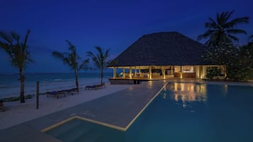 A resort with a pool, lounge chairs, and a thatched-roof building.