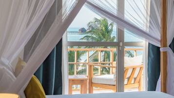 Une chambre avec un lit, une fenêtre donnant sur un balcon et des palmiers, et un baldaquin au-dessus du lit.