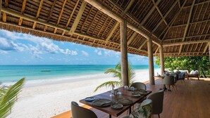 Een eetgedeelte aan het strand met een houten terras, gedekte tafels en uitzicht op de oceaan.