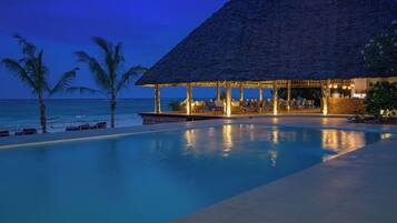 A poolside area with a thatched-roof structure, lounge chairs, and a view of the ocean.