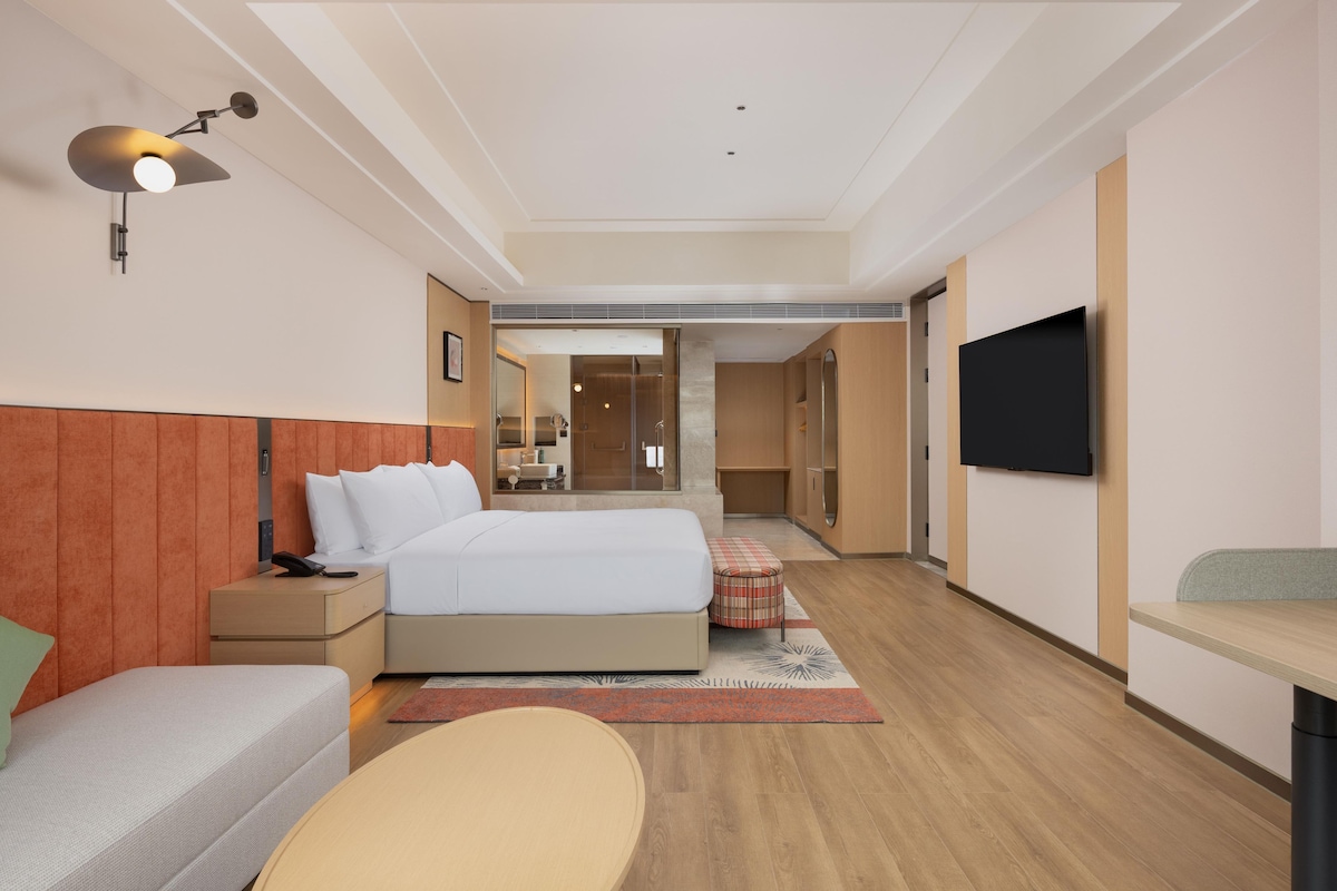 Une chambre d’hôtel moderne avec un grand lit, des tables de chevet, une télévision et une vue sur la salle de bain.