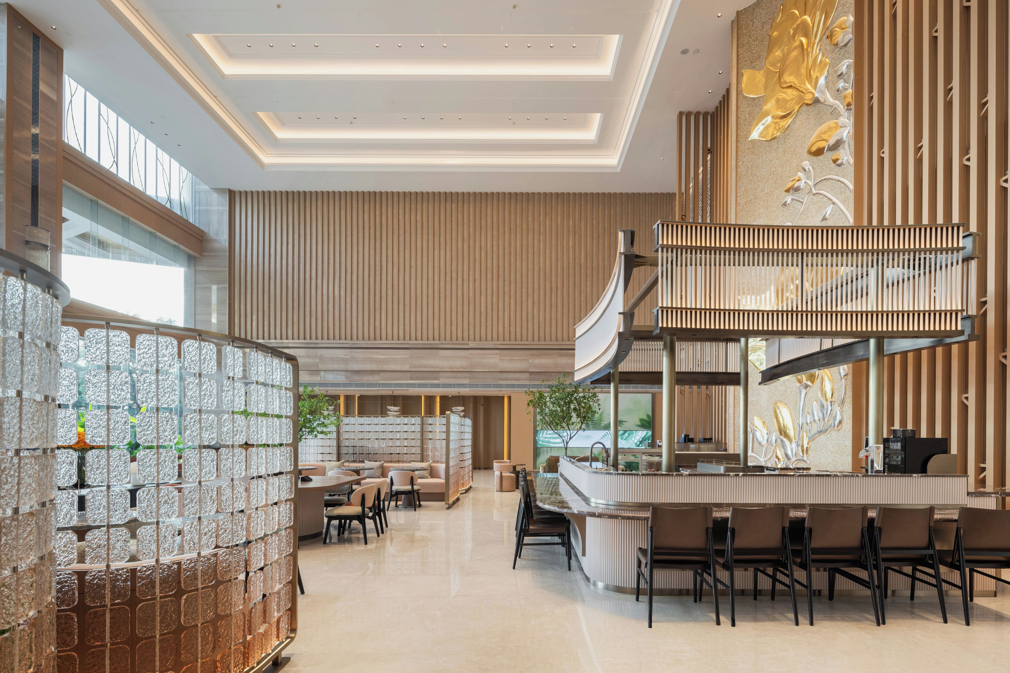 Un moderno vestíbulo de hotel con una zona de estar central, un bar y una pared decorativa con diseño dorado.