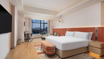 A modern hotel room with a large bed, a desk, and a view of the city.