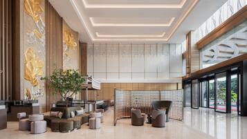 A spacious lobby with a modern design, featuring a seating area with sofas and chairs, a large tree, and a decorative wall with vertical panels.