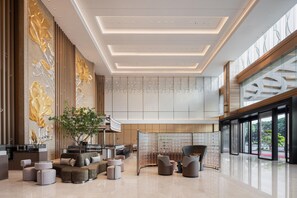 Un hall d’entrée spacieux au design moderne, comprenant un espace détente avec des canapés et des fauteuils, un grand arbre et un mur décoratif agrémenté de panneaux verticaux.