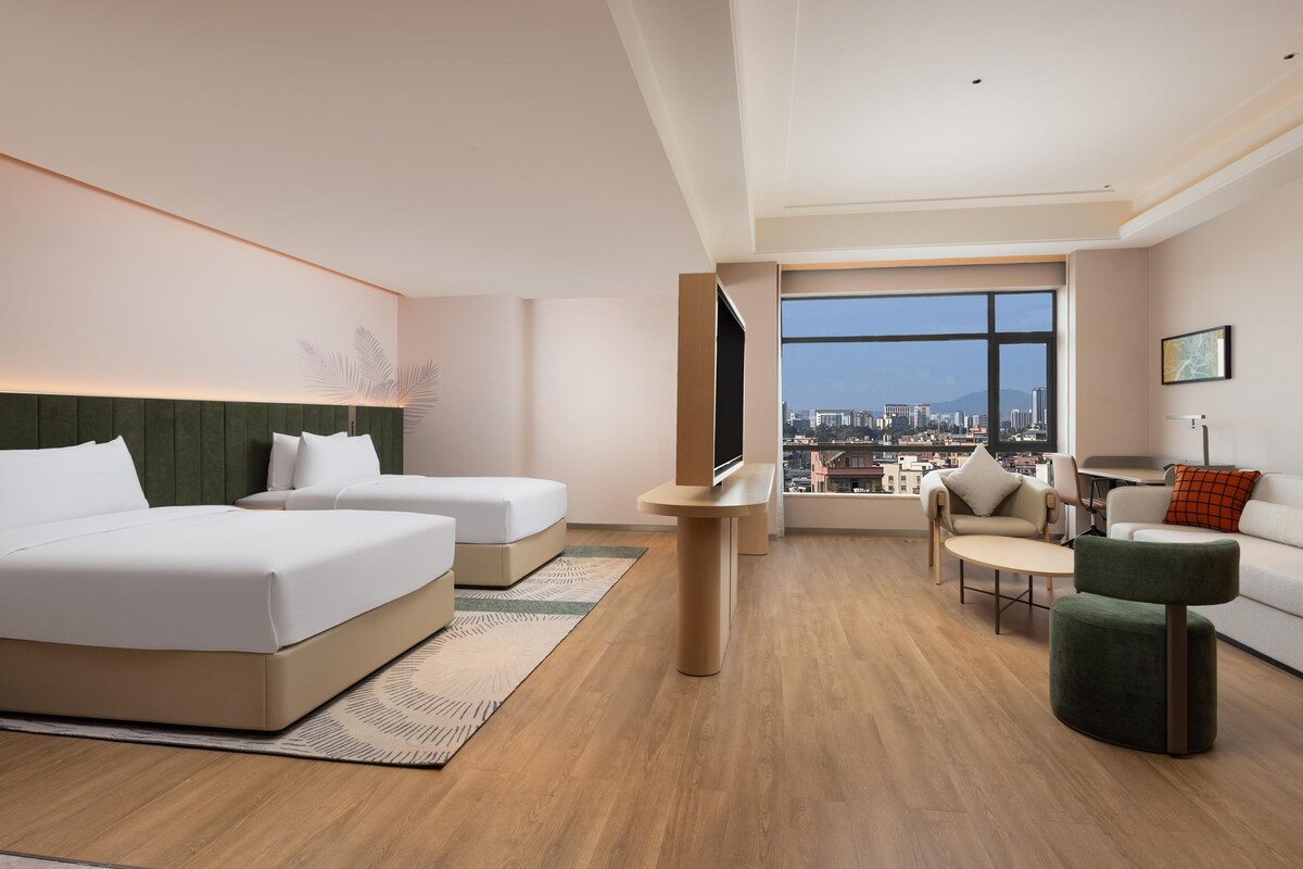 Une chambre d’hôtel moderne avec deux lits, un canapé, une petite table et une vue sur la ville.
