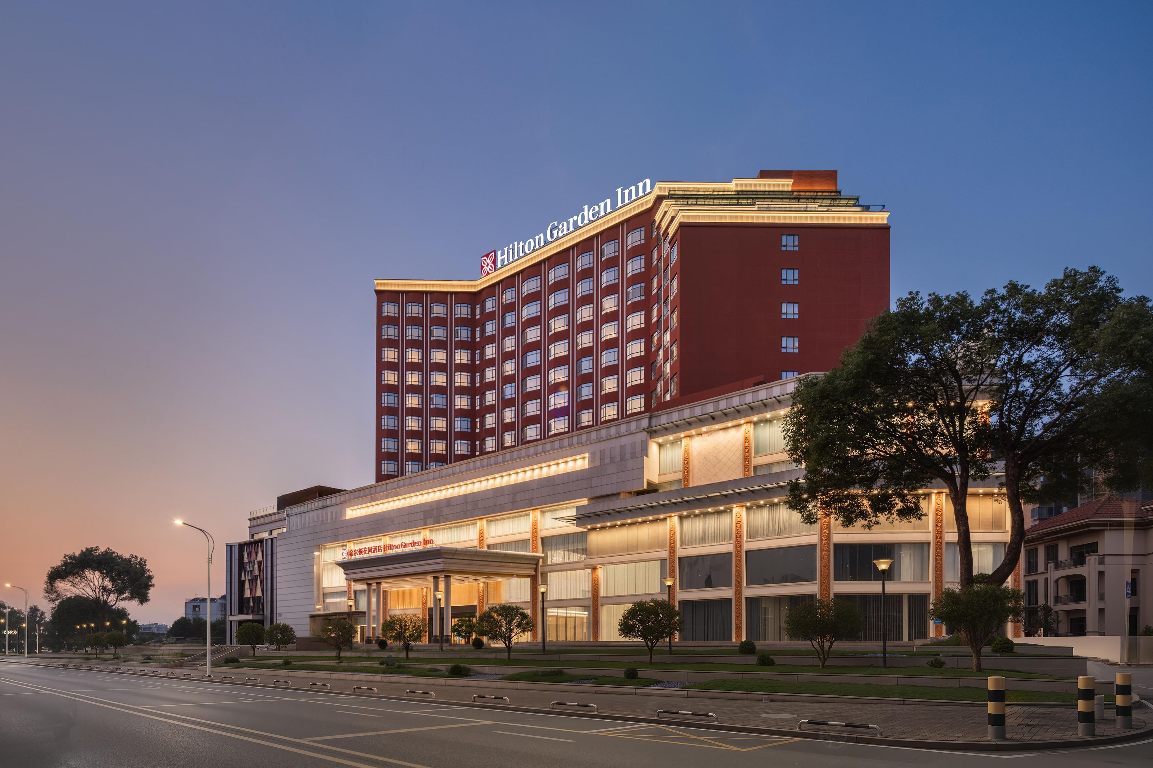 A Hilton Garden Inn hotel with a prominent red facade, multiple floors, and a well-lit entrance area.