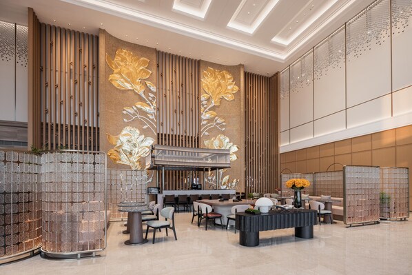 Un hall d’entrée moderne doté d’un bar central, de différents espaces aménagés pour s’asseoir et de panneaux muraux décoratifs.