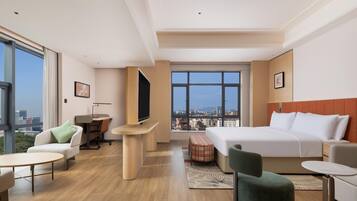 Una habitación de hotel moderna con una cama grande, un escritorio, una silla, una mesita y vistas a la ciudad a través de amplios ventanales.
