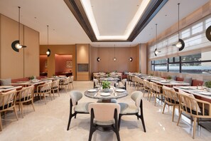 A spacious dining area with multiple round tables and chairs, large windows, and pendant lighting. - Hilton Garden Inn Dongguan Wanjiang Jiangjing Road (Dongguan)