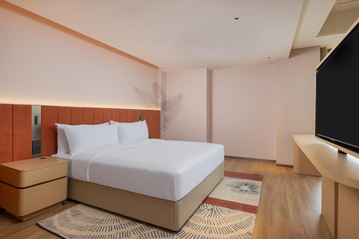Une chambre d’hôtel moderne équipée d’un lit, d’une table de chevet, d’un téléviseur et d’une plante décorative.