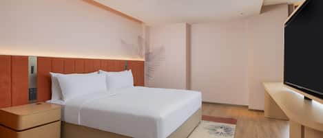 A modern hotel room with a bed, nightstand, TV, and a decorative plant.