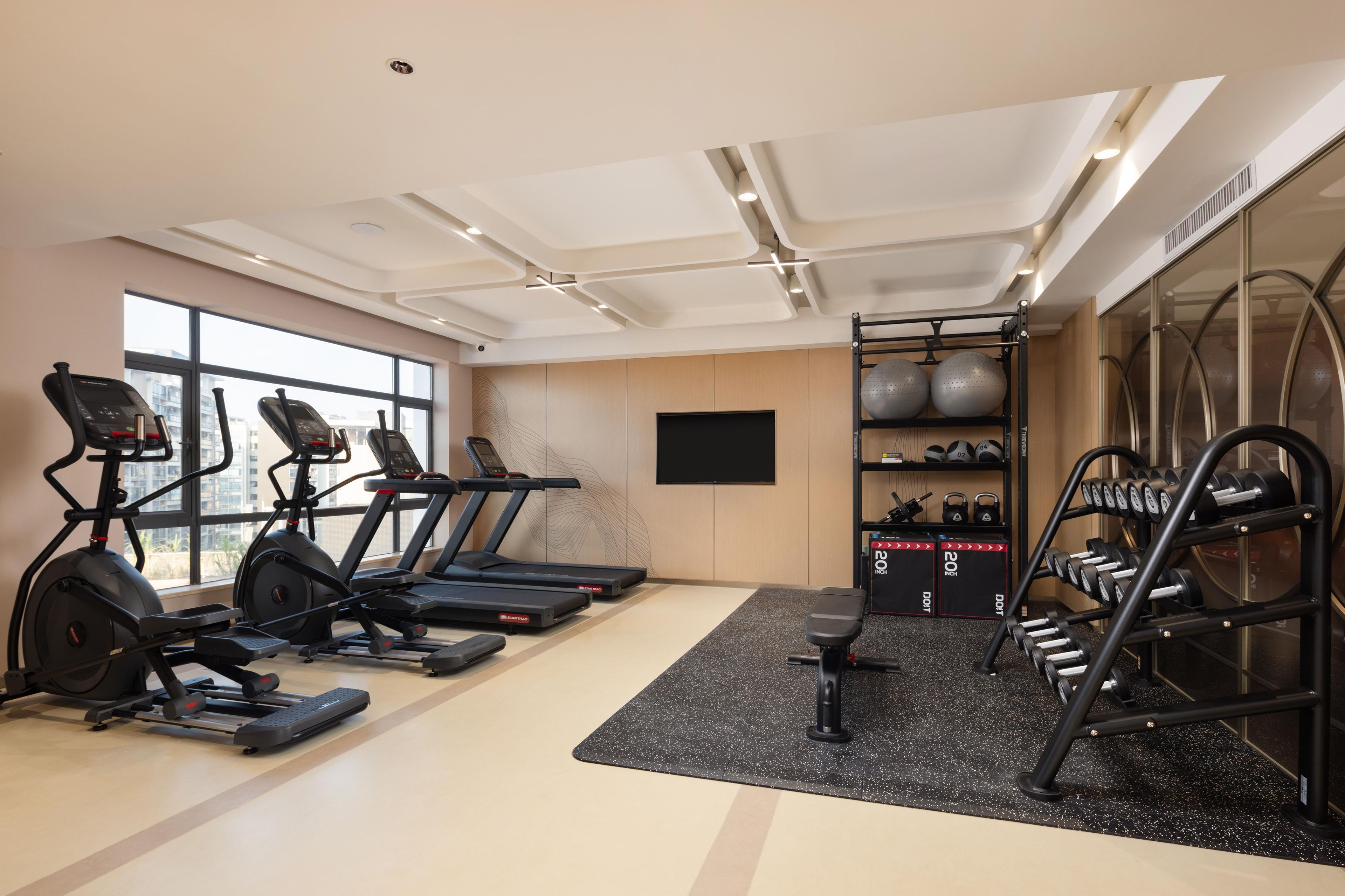 Une salle de sport équipée de tapis de course, de vélos elliptiques, d’un banc et d’un porte-haltères.