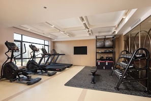Une salle de sport équipée de tapis de course, de vélos elliptiques, d’un banc et d’un porte-haltères.