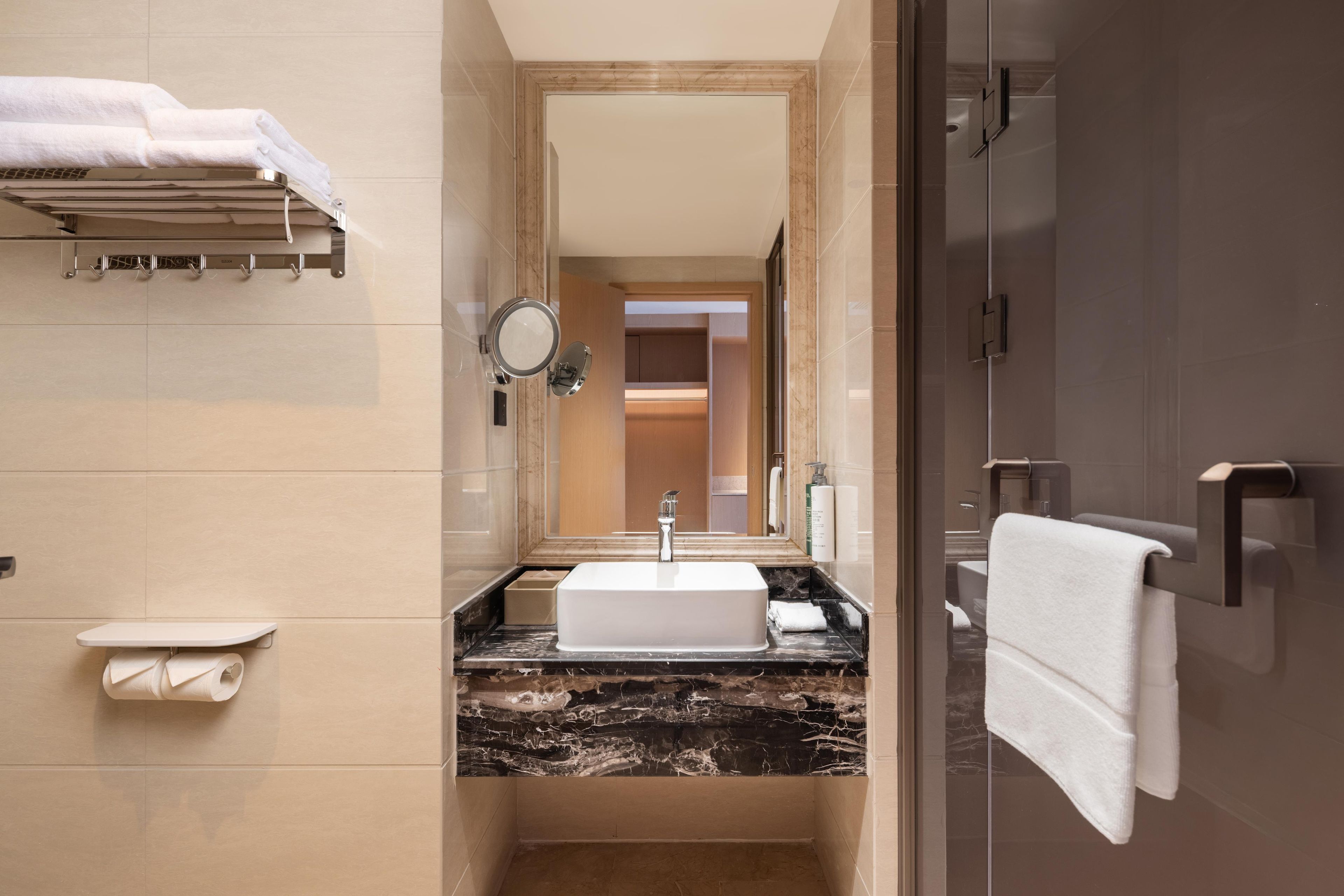 A modern bathroom with a sink, mirror, towel rack, and a toilet paper holder.