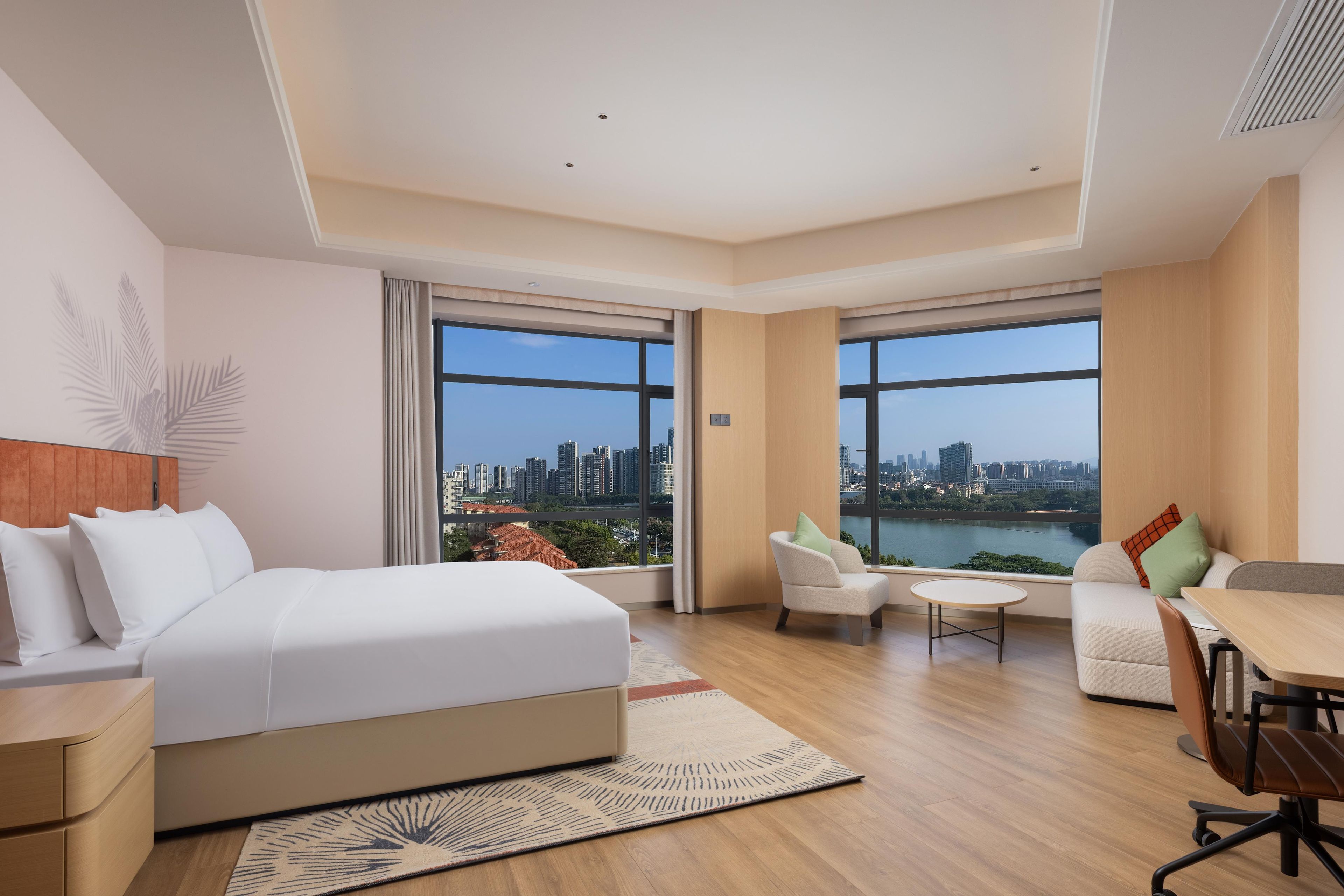Une chambre d’hôtel moderne dotée d’un grand lit, d’un coin repas et offrant une vue sur les toits de la ville et sur l’eau.