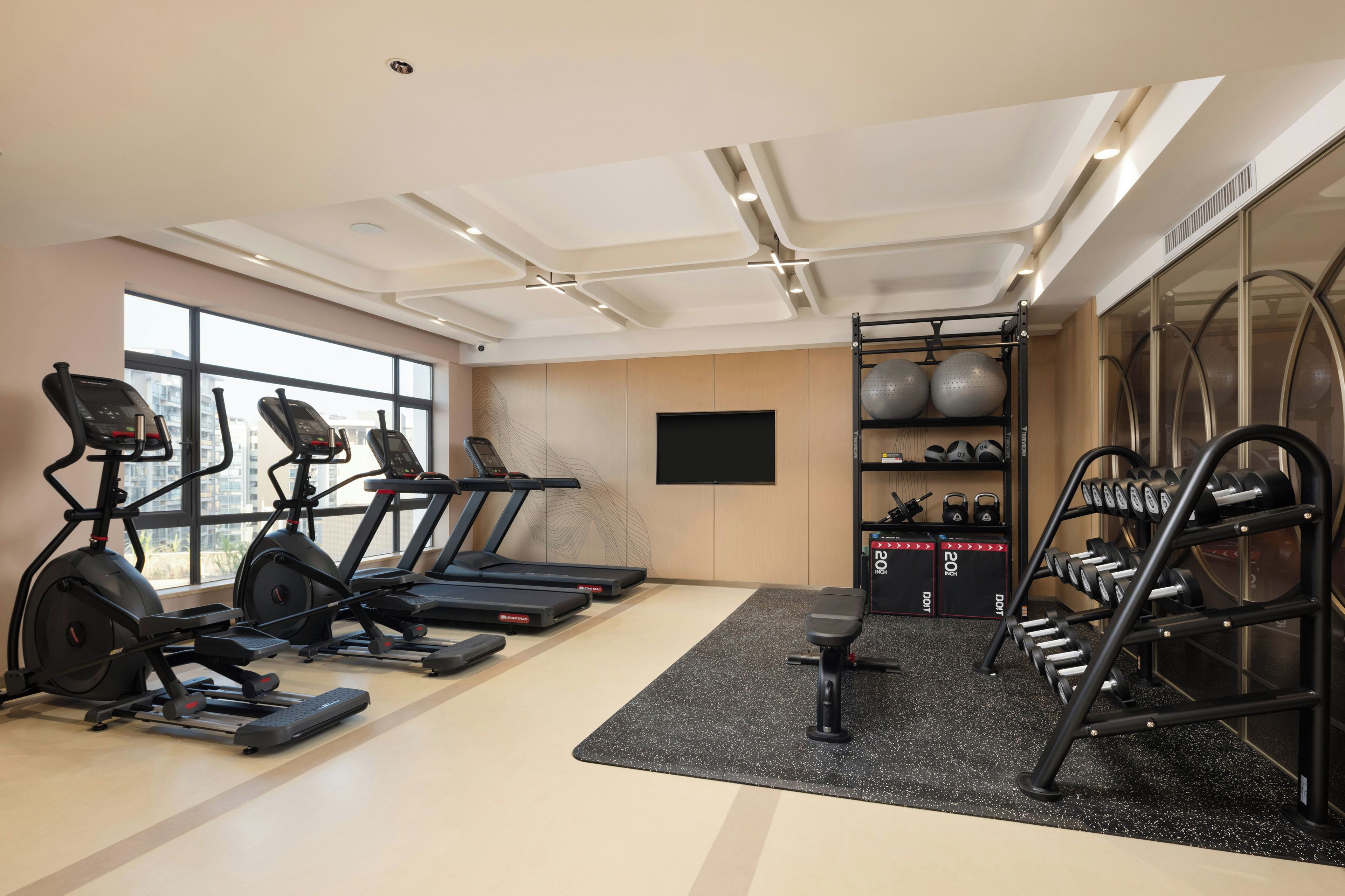 A gym with treadmills, a bench, weights, and a large window.