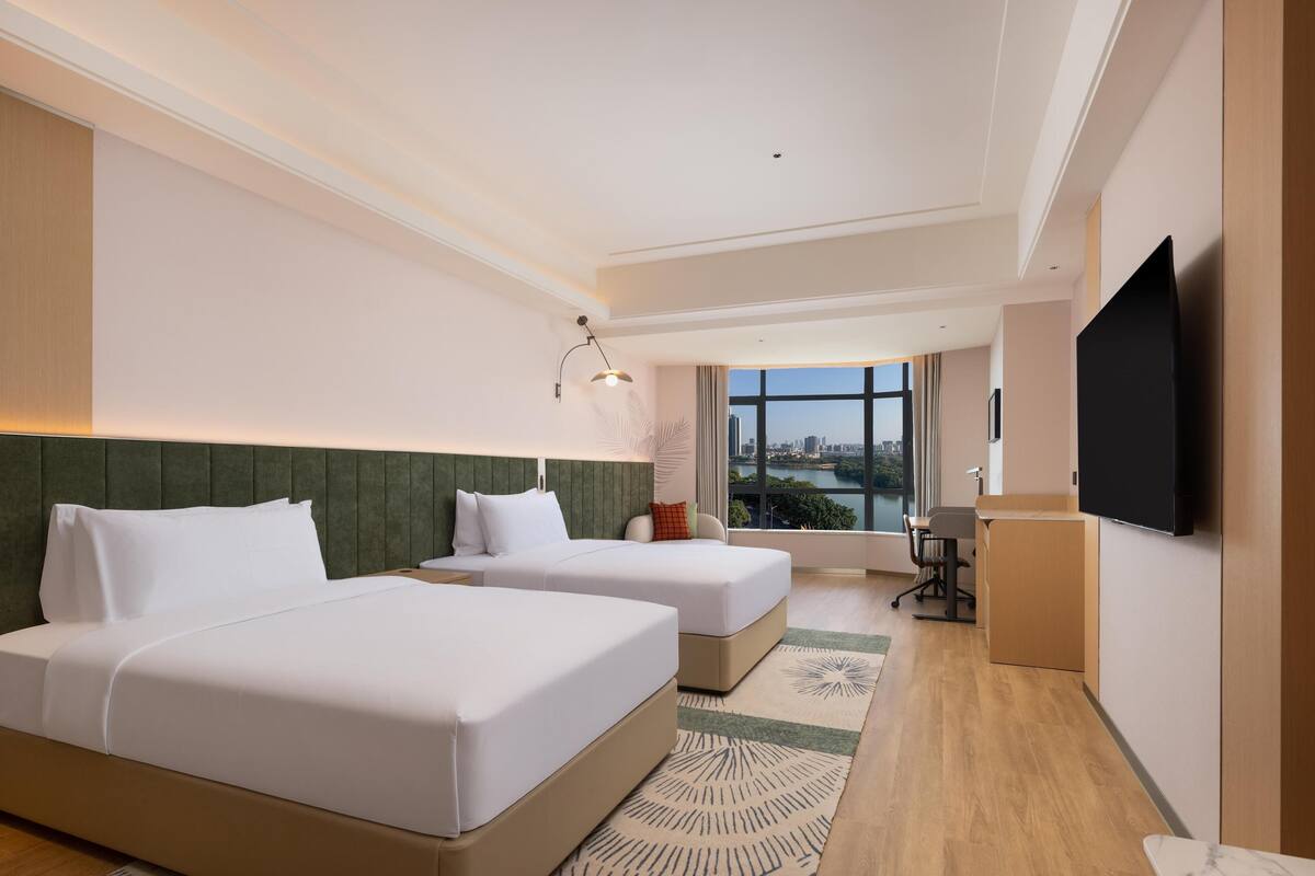 Une chambre d’hôtel moderne avec deux lits, un bureau et une grande fenêtre donnant sur la ville.
