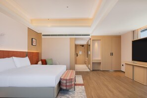 Une chambre d’hôtel avec un lit, une télévision, une armoire et une salle de bain visible à travers une porte ouverte.