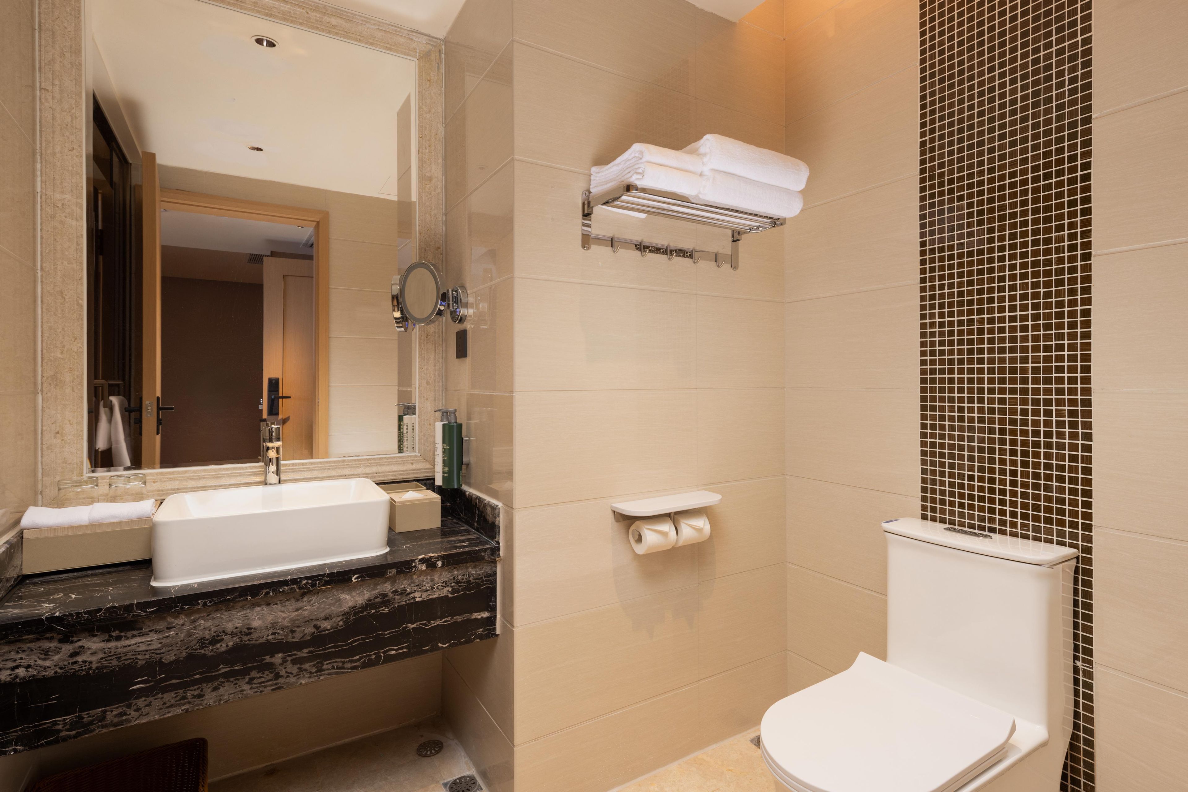 A bathroom with a sink, mirror, towel rack, toilet, and a shower area.