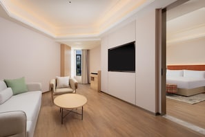 Une chambre d’hôtel moderne avec un canapé, une petite table ronde, un lit et un téléviseur fixé au mur.