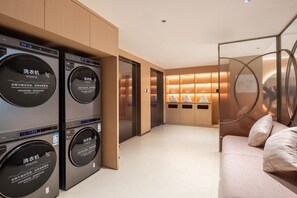 A modern laundry room with stacked washing machines, a sofa, and a glass partition. - Hilton Garden Inn Dongguan Wanjiang Jiangjing Road (Dongguan)