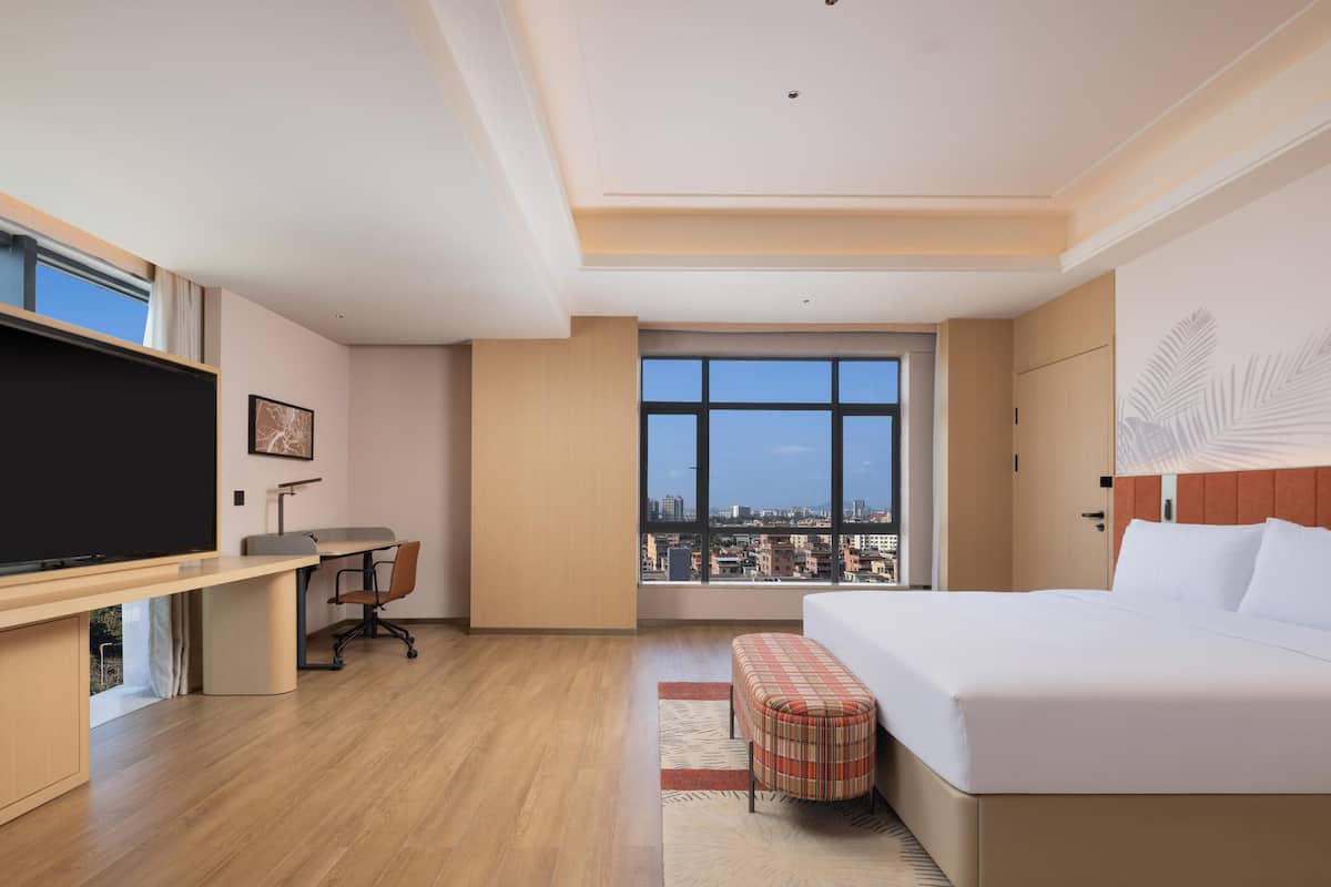 Une chambre d’h ôtel comprenant un lit, un bureau, une télévision, une fenêtre donnant sur la ville et une grande baie vitrée.