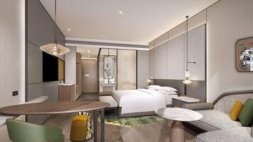 A modern hotel room with a bed, a sofa, a dining table, and a small kitchen area.