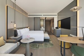 Ein modernes Hotelzimmer mit einem großen Bett, Nachttischen, einem runden Tisch, einer Couch, einem Fernseher und einer Küchenzeile.