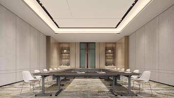 A conference room with a long table, white chairs, a patterned carpet, and a modern ceiling design.
