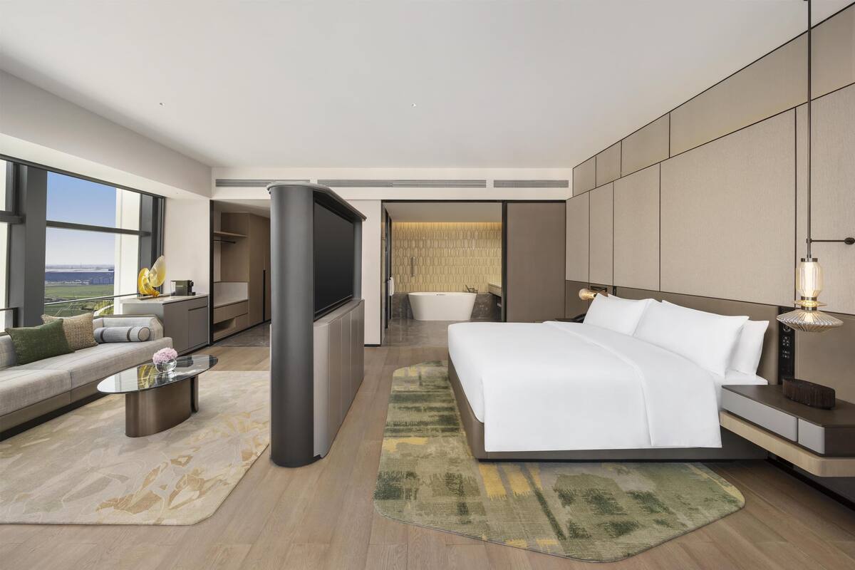 Une chambre d’hôtel moderne dotée d’un grand lit, d’un canapé, d’une télévision et d’une baignoire, et offrant une vue sur la ville.