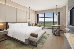A modern hotel room with a large bed, bedside tables, a desk, a chair, a TV, and a view of the city. - Doubletree by Hilton Zhengzhou Airport Aerotropol (Zhengzhou)