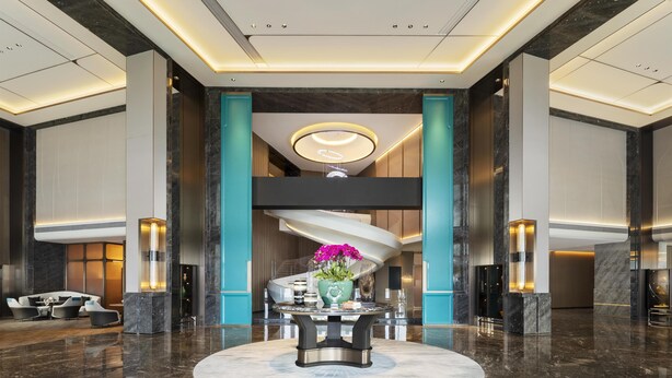 Een moderne lobby met een ronde centrale tafel, zithoek en een spiraaltrap.