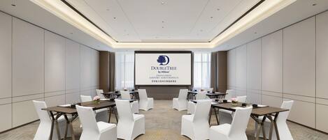 A conference room with a large screen displaying the DoubleTree by Hilton logo, white chairs, and a carpeted floor.