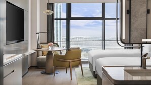 Een moderne hotelkamer met een groot bed, een eettafel, een bank, een televisie en uitzicht op de stad.