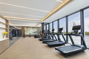 A modern gym with treadmills aligned along a wall with large windows, a wooden floor, and exercise equipment in the background. - Doubletree by Hilton Zhengzhou Airport Aerotropol (Zhengzhou)