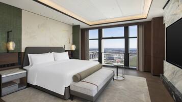 A modern hotel room with a large bed, bedside tables, a flat-screen TV, and a view of the cityscape.
