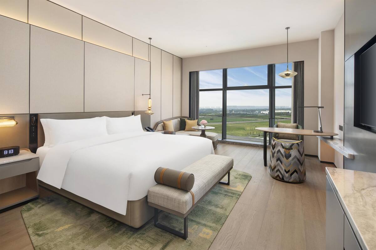 Une chambre d’hôtel moderne, dotée d’un grand lit, de tables de chevet, d’un bureau, d’une chaise, d’une télévision et offrant une vue sur la ville.