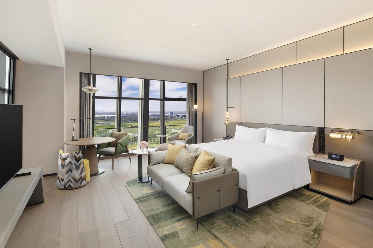 Une chambre d’hôtel moderne, dotée d’un grand lit, d’un canapé, d’un bureau et offrant une vue sur le paysage urbain.